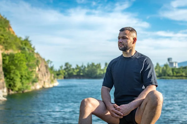 Taş ocağının arka planında kayaların üzerinde oturan sakallı genç adam. Yakışıklı portre..
