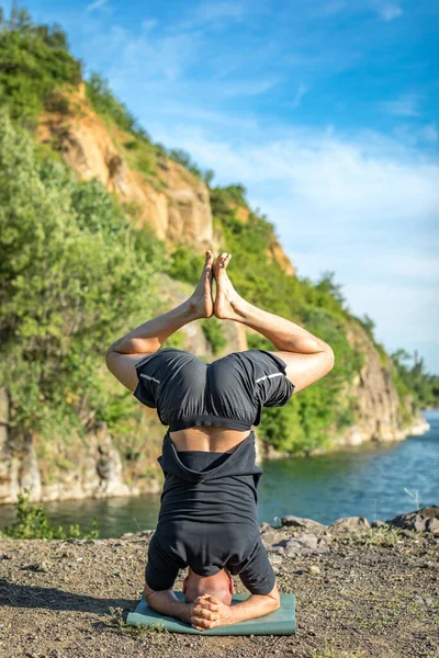 Sakallı, yakışıklı, siyah saçlı, yoga yapan bir adam. Kafasının üstünde duran genç adam Sirshasana 'nın taş ocağı gölünde durduğu pozda..