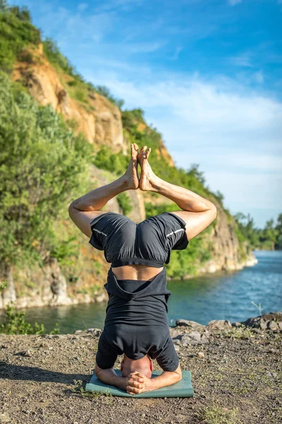 Sakallı, yakışıklı, siyah saçlı, yoga yapan bir adam. Kafasının üstünde duran genç adam Sirshasana 'nın taş ocağı gölünde durduğu pozda..