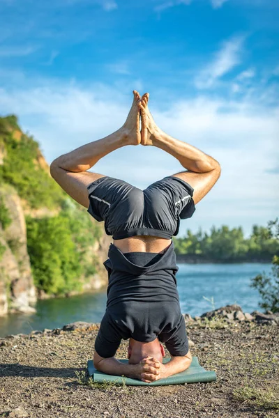 Sakallı, yakışıklı, siyah saçlı, yoga yapan bir adam. Kafasının üstünde duran genç adam Sirshasana 'nın taş ocağı gölünde durduğu pozda..