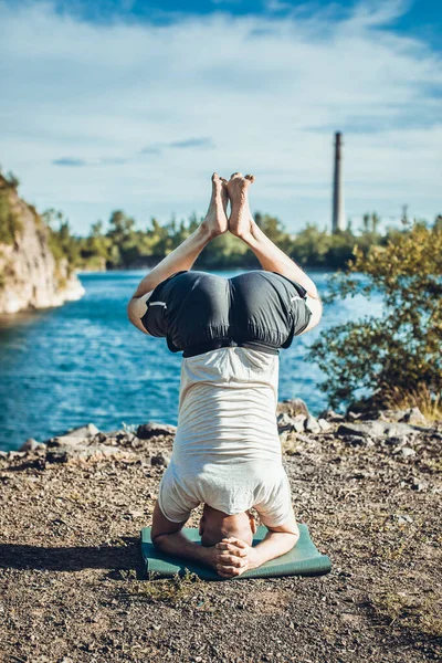 Sakallı, yakışıklı, siyah saçlı, yoga yapan bir adam. Kafasının üstünde duran genç adam Sirshasana 'nın taş ocağı gölünde durduğu pozda..