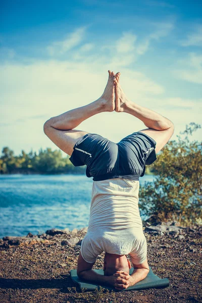Güçlü sağlıklı atletik adam sabah antrenmanı yapıyor taş ocağı gölünde yoga yapıyor, baş aşağı duruyor. Rahatlama ve meditasyon, sağlıklı yaşam tarzı konsepti. Uluslararası Yoga Günü.