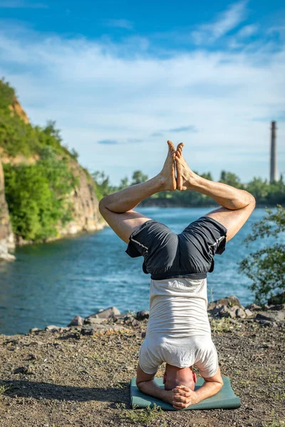 Güçlü sağlıklı atletik adam sabah antrenmanı yapıyor taş ocağı gölünde yoga yapıyor, baş aşağı duruyor. Rahatlama ve meditasyon, sağlıklı yaşam tarzı konsepti. Uluslararası Yoga Günü.