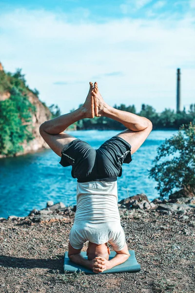 Güçlü sağlıklı atletik adam sabah antrenmanı yapıyor taş ocağı gölünde yoga yapıyor, baş aşağı duruyor. Rahatlama ve meditasyon, sağlıklı yaşam tarzı konsepti. Uluslararası Yoga Günü.