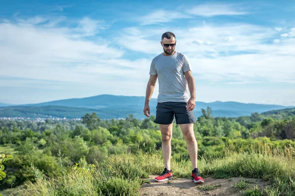 Genç sakallı gezgin ayakları arkasında günbatımı dağlarıyla tek başına duruyor. Yaşam tarzı seyahat kavramı.