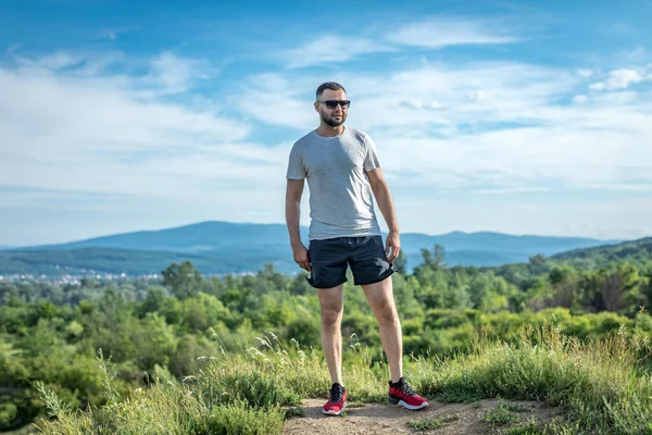 Genç sakallı gezgin ayakları arkasında günbatımı dağlarıyla tek başına duruyor. Yaşam tarzı seyahat kavramı.