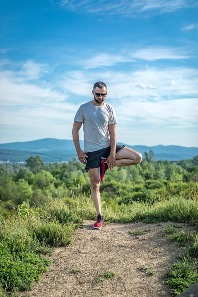 Genç sakallı gezgin ayakları arkasında günbatımı dağlarıyla tek başına duruyor. Yaşam tarzı seyahat kavramı.