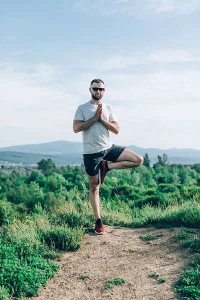 Genç sakallı gezgin ayakları arkasında günbatımı dağlarıyla tek başına duruyor. Yaşam tarzı seyahat kavramı.
