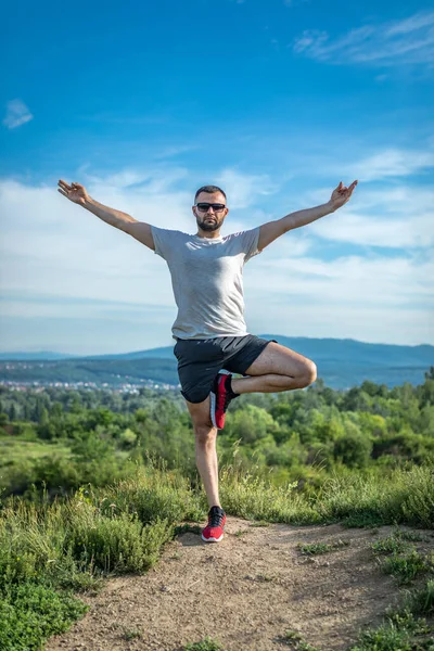 Genç sakallı gezgin ayakları arkasında günbatımı dağlarıyla tek başına duruyor. Yaşam tarzı seyahat kavramı.
