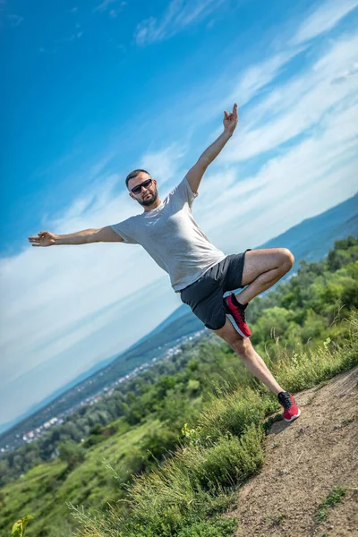 Genç sakallı gezgin ayakları arkasında günbatımı dağlarıyla tek başına duruyor. Yaşam tarzı seyahat kavramı.