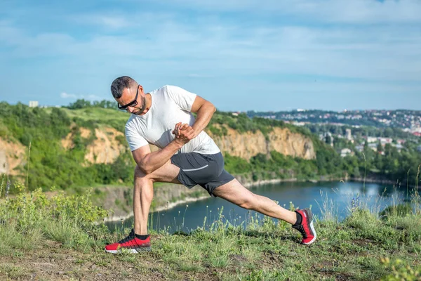 Profesyonel fitness eğitmeni. Sakallı sporcu antrenman yapıyor, taş ocağı gölünde geriniyor. Açık hava spor konsepti.