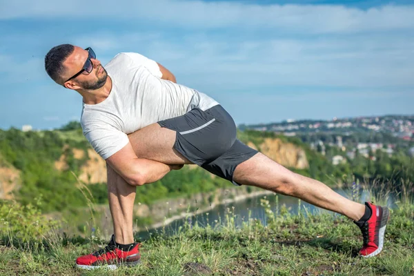 Profesyonel fitness eğitmeni. Sakallı sporcu antrenman yapıyor, taş ocağı gölünde geriniyor. Açık hava spor konsepti.
