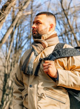 Parktaki sakallı adam. Ormanda genç bir gezgin. Sırt çantası ve ceketi olan yalnız bir adam. Sonbahar parkında siyah sakallı, yetişkin bir adam..