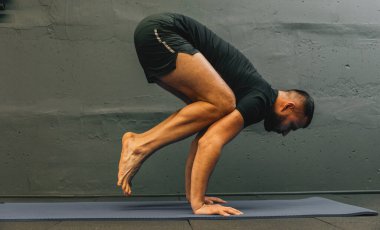 Sportif genç adam amuda kalkma yogası yapıyor. Fotokopi alanı için gri arkaplan ile kentsel fitness salonunda stüdyo çekimi.