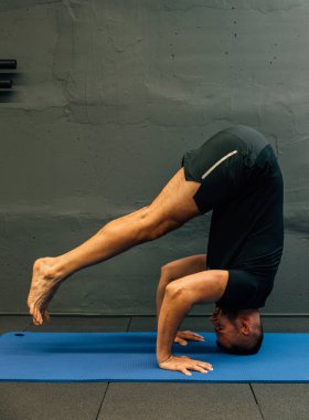 Sportif genç adam amuda kalkma yogası yapıyor. Fotokopi alanı için gri arkaplan ile kentsel fitness salonunda stüdyo çekimi.