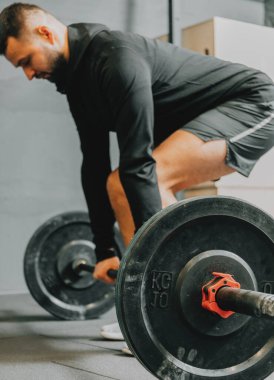 Spor kıyafetli genç bir adam spor salonunda antrenman yaparken ağırlık kaldırmaya hazırlanıyor. Fitness sporu veya sağlıklı yaşam tarzı konsepti.
