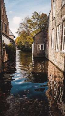 Bruges, Belçika 'dan açık hava manzarası. Brugge şehir merkezindeki nehir suyunda güzel bir yansıma. Tuğla binalar ve karanlık karamsar renkler, köprüden manzara. Popüler hedef