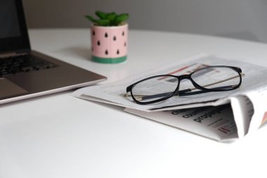 İzolasyon için merkez ofis çalışma alanı. Evde eğitim ya da serbest meslek edinmek için öğrenim yeri. Boş yeri olan beyaz masa. Gri dizüstü bilgisayarın yanında gazete ve gözlük. Evde eğitim.