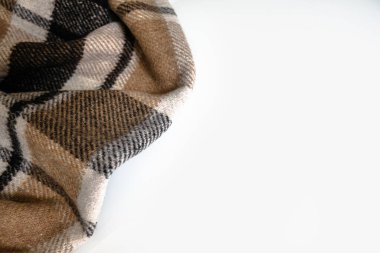 Beyaz bir masa üzerinde geometrik desenli buruşuk ekose battaniye. Kopya için boş alan. Yaşam tarzı için kahverengi katlanmış köşe. Soğuk hava için yumuşak yün malzeme. Sıcak ve rahat tekstil hissi.