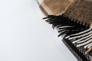 Beyaz bir masanın üzerinde, geometrik desenli katlanmış ekose bir battaniye. Kopya için boş alan. Kahverengi köşeleri yaşam tarzı için katlıyor. Soğuk hava için yumuşak yün malzeme. Sıcak ve rahat tekstil.
