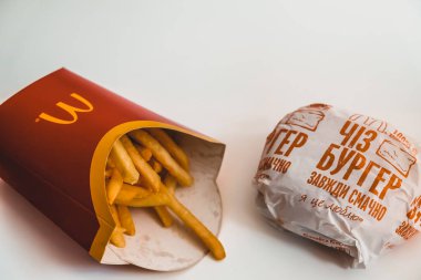 Lviv / Ukrayna - Nisan 2020: McDonald 's patates kızartması ve çizburger evdeki beyaz masada. Koronavirüs salgını sırasında sağlıksız yiyecekler. Tecritteyken yemek siparişi vermek. Beyaz boşluk kaldı.