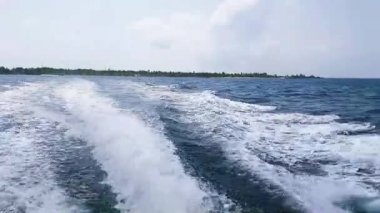 Hint Okyanusu 'ndaki motorlu teknenin arkasında beyaz köpüklü su izi. Maldivler 'deki adadan hızlı tekne yolculuğu. Hız feribotundan bir deniz yüzeyindeki dalgalardan sıçrama.