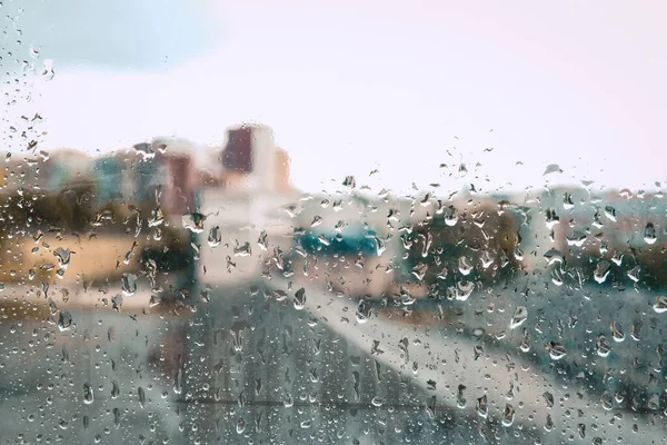 City view through the wet window on a rainy day. Stay home in daylight during social isolation. Blurred cityscape in a poor weather conditions. Moisture spray and rain drops on a glass surface indoors