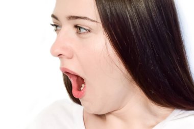 Beyaz arka planda esneyen beyaz bir kızın portresi. Genç, uzun saçlı kadın ağzı açık esniyor..