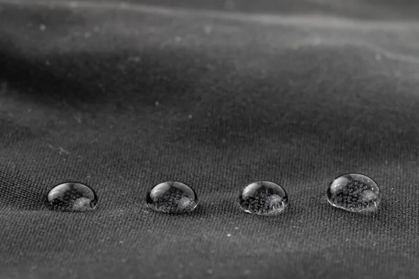 Line of four water beads on water repellent fabric