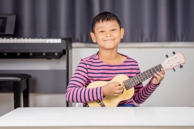Asyalı çocuk yaş 7-8 oyun ukulele odasında, tutkulu aşk müzik, çocuk geliştirme kavramı