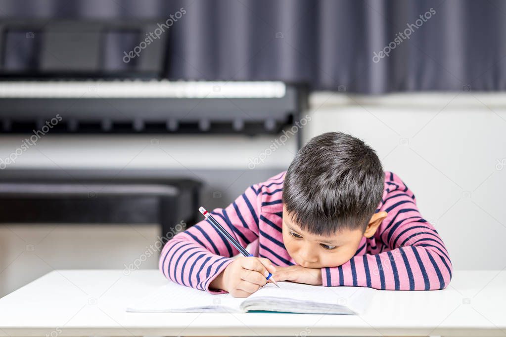 Young Asian boy tired write on the note book by pencil in the room