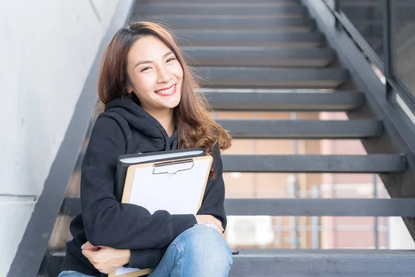 年轻学生女性坐在台阶与文件夹和拷贝书在校园区域 — 图库照片