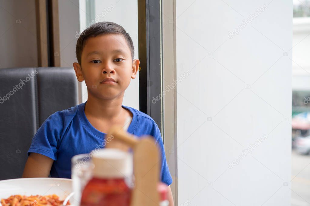 Cute asian boy seat at window eating food in a restaurant