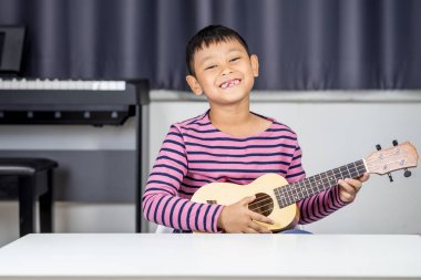 Asyalı çocuk yaş 7-8 oyun ukulele odasında, tutkulu aşk müzik, çocuk geliştirme kavramı