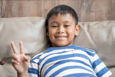 Asyalı küçük çocuk oturup barış kaydolun tutan Divan