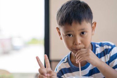 Asyalı küçük çocuk bir barış işareti tutarak su emme.