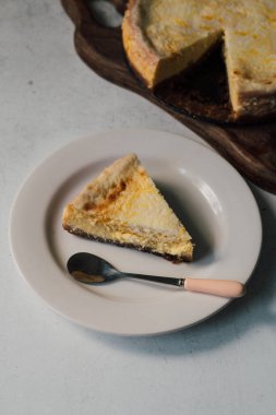 Lezzetli bir dilim ev yapımı mango limonlu cheesecake, arka planda kalan turtayla birlikte beyaz bir tabakta. Organik malzemelerden lezzetli bir tatlı. Aşçılık sınıfı veya yaşam tarzı günlüğü.