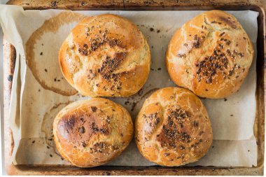 Hamburger için taze pişmiş lezzetli çörekler, üzerine sağlıklı tohumlar serpiştirilmiş, fırın tepsisi üzerinde. Ev yapımı ekmek, amatör şef tarafından pişirilmiş, ya da kahvaltıda lezzetli, zengin brioche. Genel Görünüm