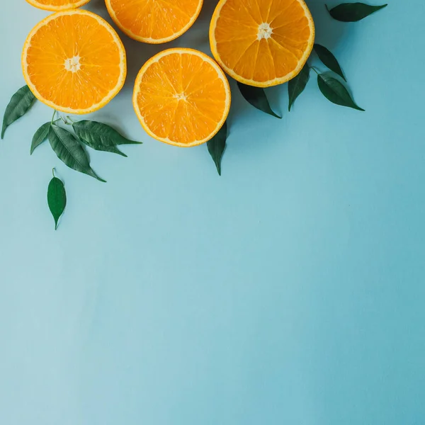 鮮やかな青を背景に おいしいハーフカットオレンジと緑の葉から創造的なフラットレイアウト 健康的で活発なライフスタイル 夏の波の概念 最小構成を表示します カラフルで幸せなレイアウト ロイヤリティフリーのストック画像