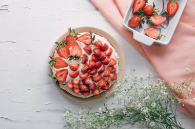 Bahçe çiçekleri ve pembe masa örtüsüyle beyaz masada nefis taze çilekli pasta. Yemek kursu ya da sağlıklı yaşam tarzı için renkli, modern bir daire. Organik malzemelerden lezzetli meyveli tart..