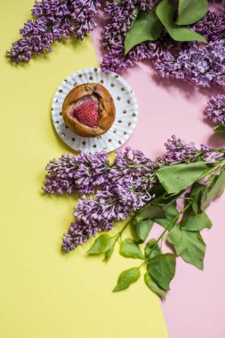 Modaya uygun bir arka planda, leylak çiçekli şekersiz çilekli kek. Fırın ya da aşçılık okulu afişi. Yaşam tarzı blog konsepti. Asgari düzeyde. Düz konum, üst görünüm bileşimi.