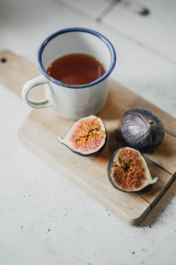 Tahta mutfak tahtasındaki incirleri bir fincan çayla yeni ikiye ayırdım. Sağlıklı ve lezzetli kahvaltı ya da aperatif, lif, mineral ve manganez açısından zengin. Seçici odaklanma, yemek pişirme veya yaşam tarzı blogu.