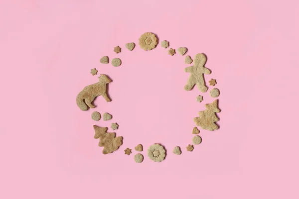 Holidays spirit and nature concept: gingerbread, season biscuits shaped as fir tree with fox, man, stars and moon circle frame on pink. Cute greetings card. Creative flat lay. Top view, copy space.