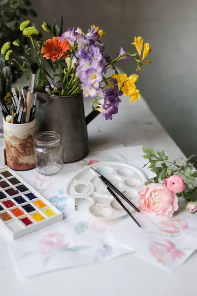 花瓶に春の花とインテリアワークスペース 紙に花を描いた 水彩パレットやブラシなどのアート用品 アーティストスタジオまたは画家の白いテーブル ストックフォト