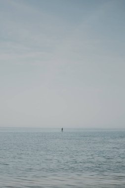 Sakin suyu olan en az deniz manzarası ve ufuk çizgisine yakın biri ayakta kürek çekerek sabahın tadını çıkarıyor. Turistler için dinlendirici ve eğlenceli yaz aktiviteleri. Aktif insanlar için deniz kenarı sporu.
