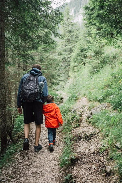 Father and son hiking on a mountain woods trail. Fun outdoor family activities in the summer. Active and healthy lifestyle. Early years education. Good parenting. Learning to embrace and enjoy nature.