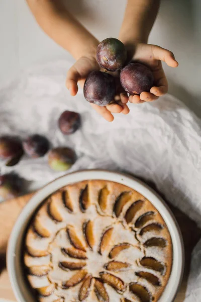 Mãos Segurando Ameixas Orgânicas Cruas Sobre Mesa Com Deliciosa Torta — Fotografia de Stock