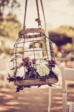Açık hava düğün töreninin dekorasyonunda içinde çiçekler ve mumlar olan kafes..