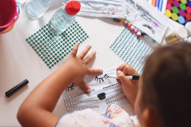 Bir kızın çalışma masasının zenital planı bir kavanoz jelle kedi maskesi boyamak.