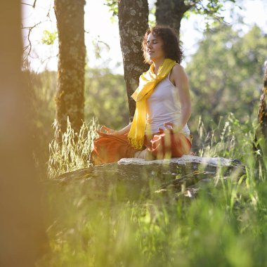 Gün batımında ağaçların arasında meditasyon yapan genç bir kadın..